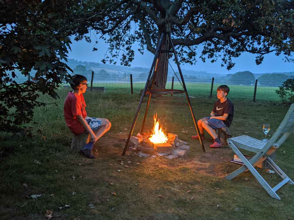 Two boys sitting around early evening Campfire, cooking on Tripod at Freshwinds Camping, Sussex