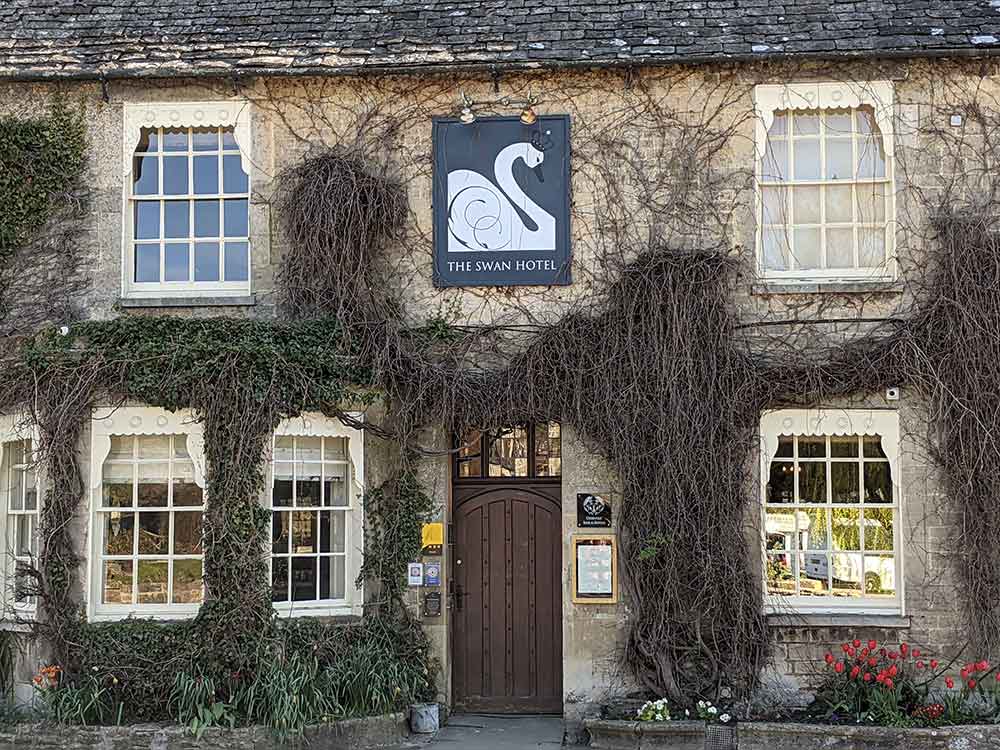 Historic hotel with wooden door and plants on the walls at front of building. An image of a swan is above the door.