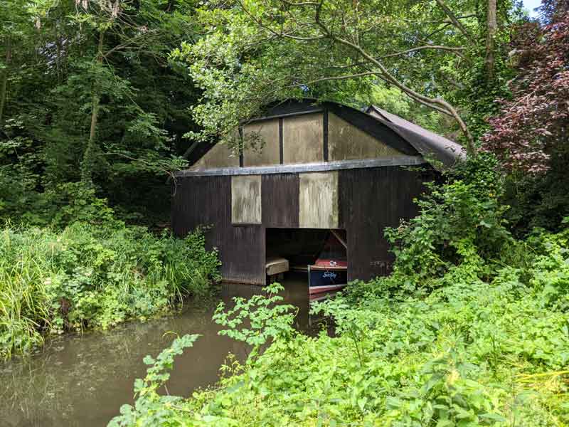 boat on water poking out of boat house, with lots of green plants and trees around