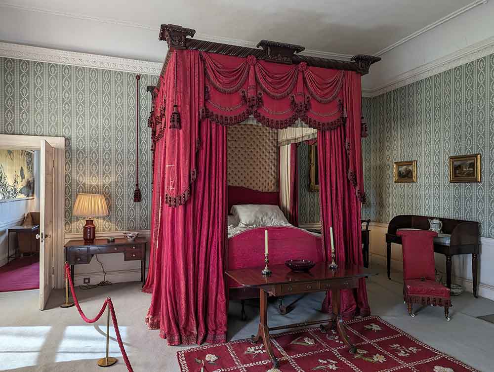 Four poster bed with red bedding and carpets, red rug and red chair