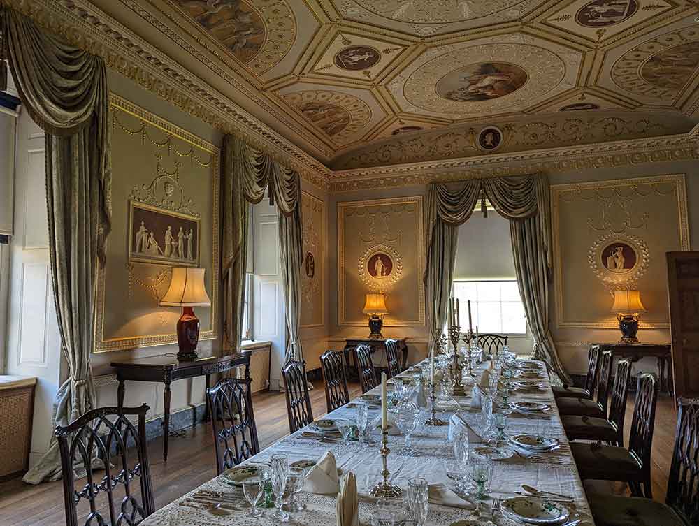 Formal dining rom laid for dinner in stately home. Exquisite paintings on ceiling.