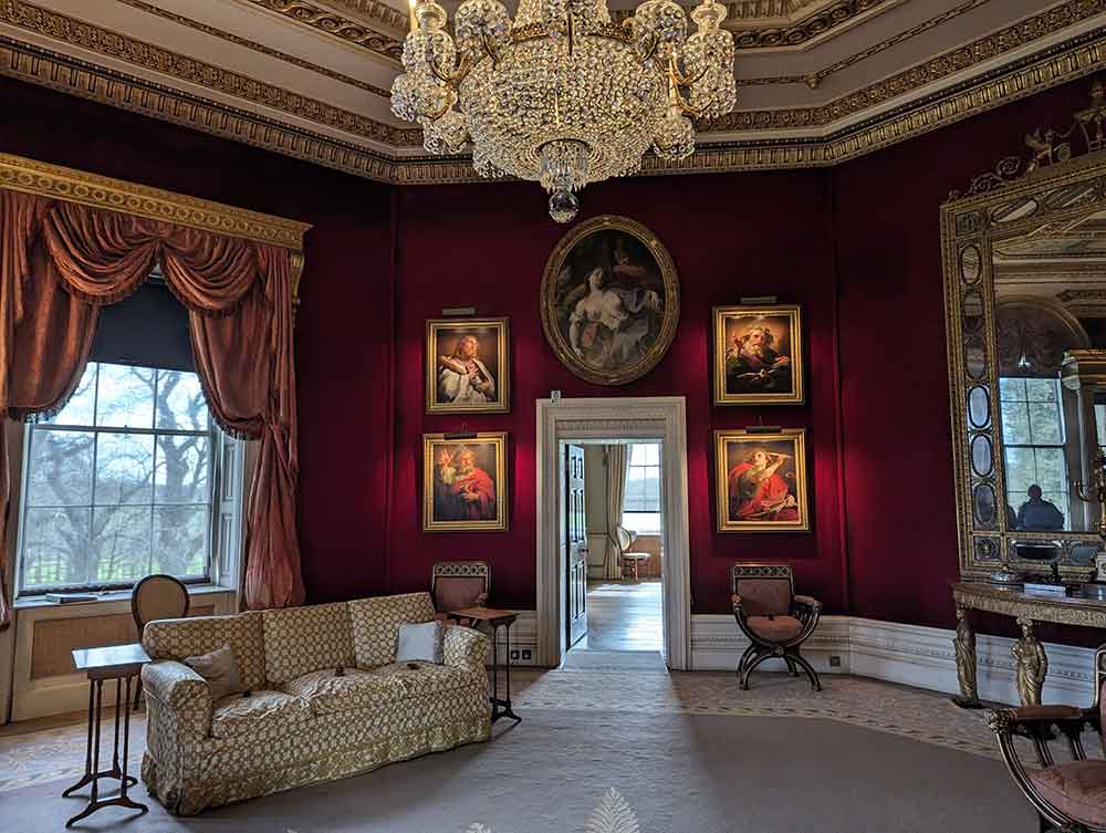 Drawing room in stately home, with red walls, high ceilings, sofa, chandelier and paintings on walls