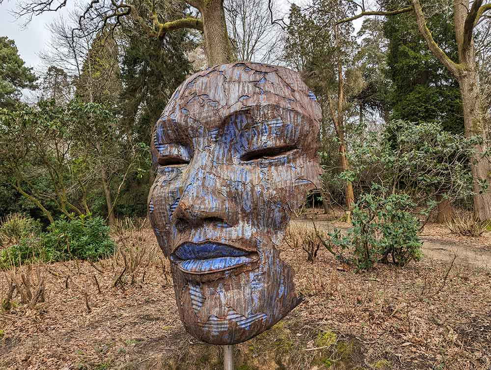 Large sculpture of face blending into to woodland landscape