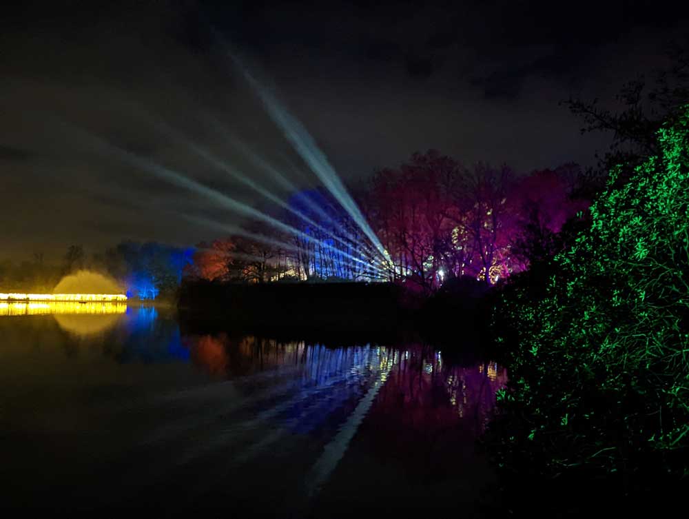 Beams of light shooting into sky and reflected on lake