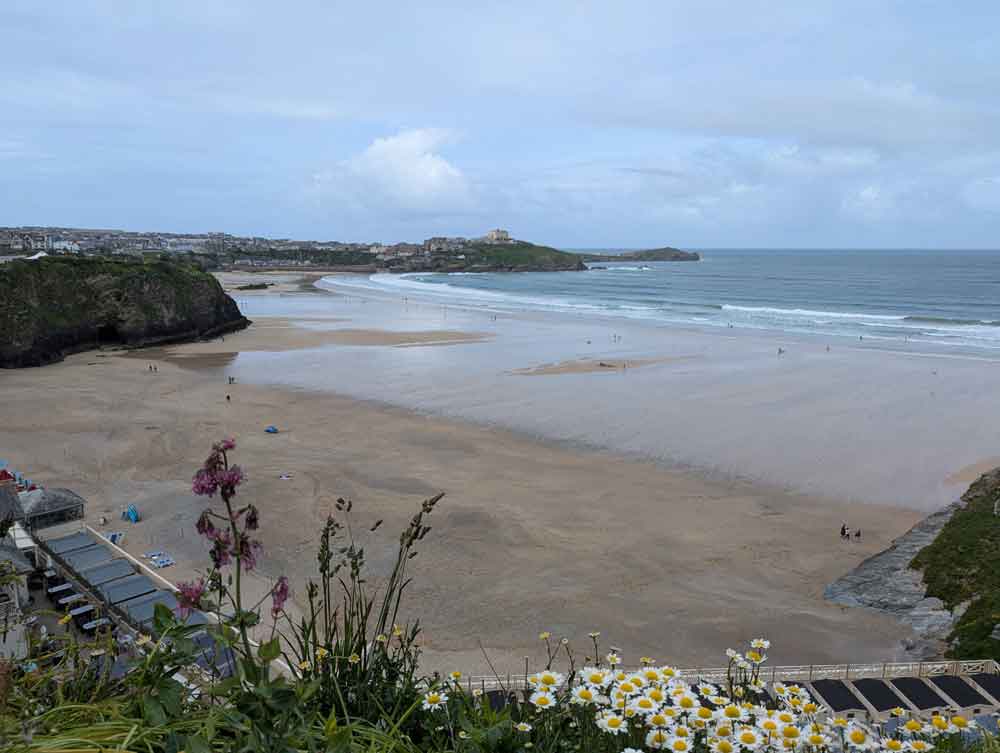 Views over Newquay Beach with golden sand and sea going out leaving a wet mark