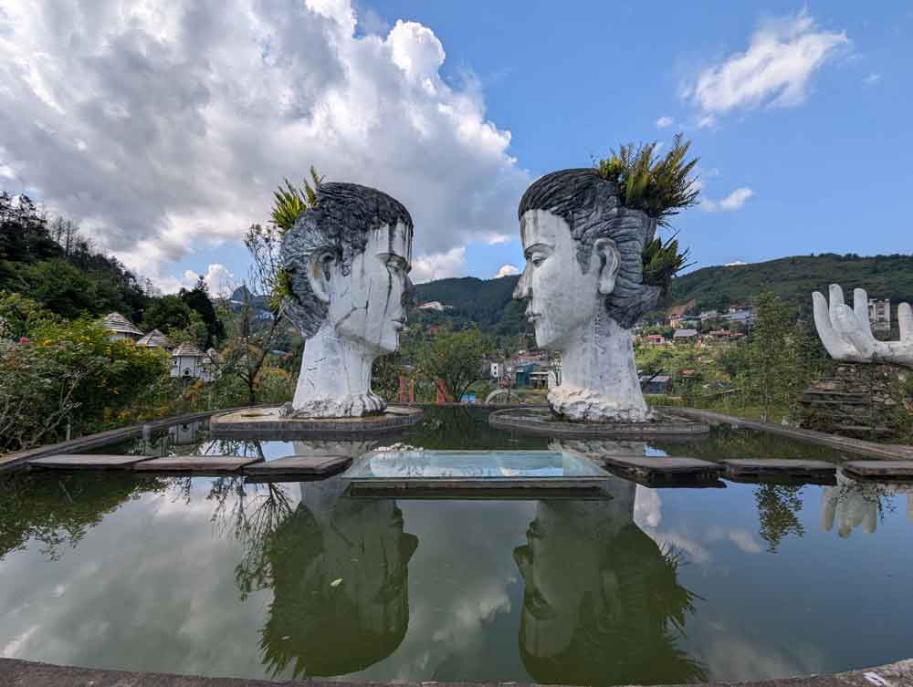 2 large statues of heads facing in each and reflected in the pool in front. (at Swing Sapa in Sapa, Vietnam) Blue sky with fluffy clouds.