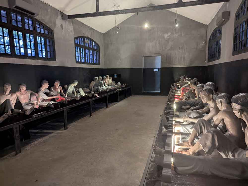 Rows, of prisoners on low benches as Hoa Lo Prison, Hanoi