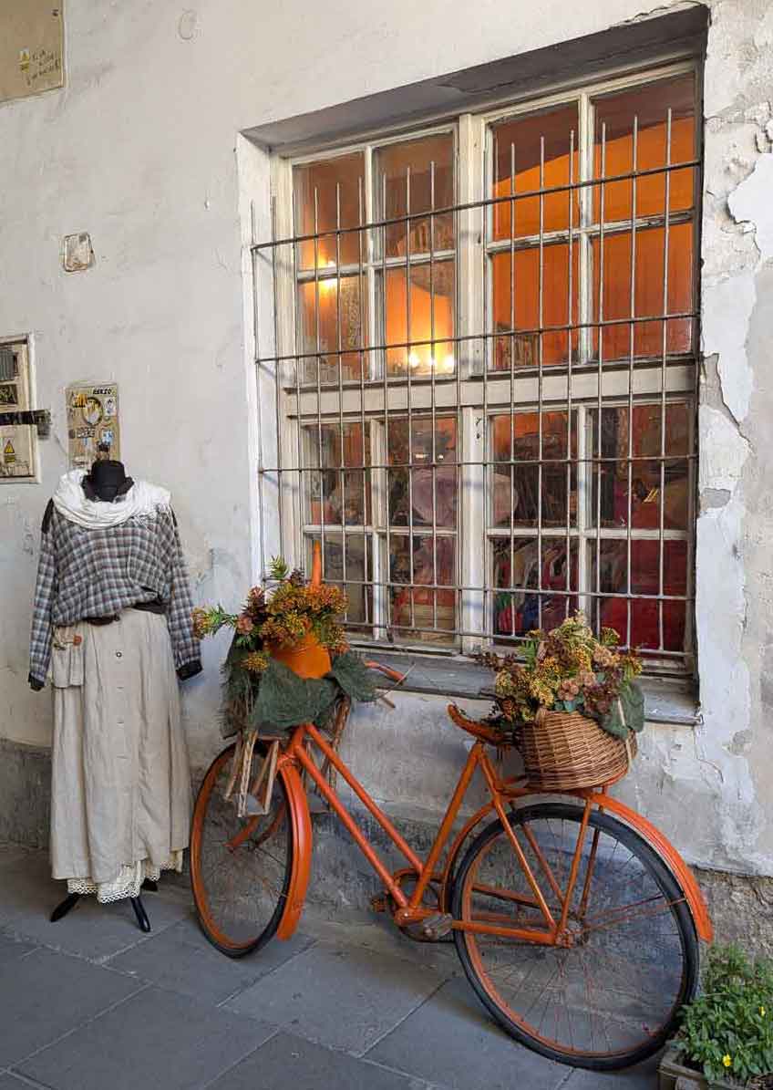 Orange bike with flowers in basket and mannequin with old clothes in front of a window with grilles on In Schindler's Passage, Kazimierz