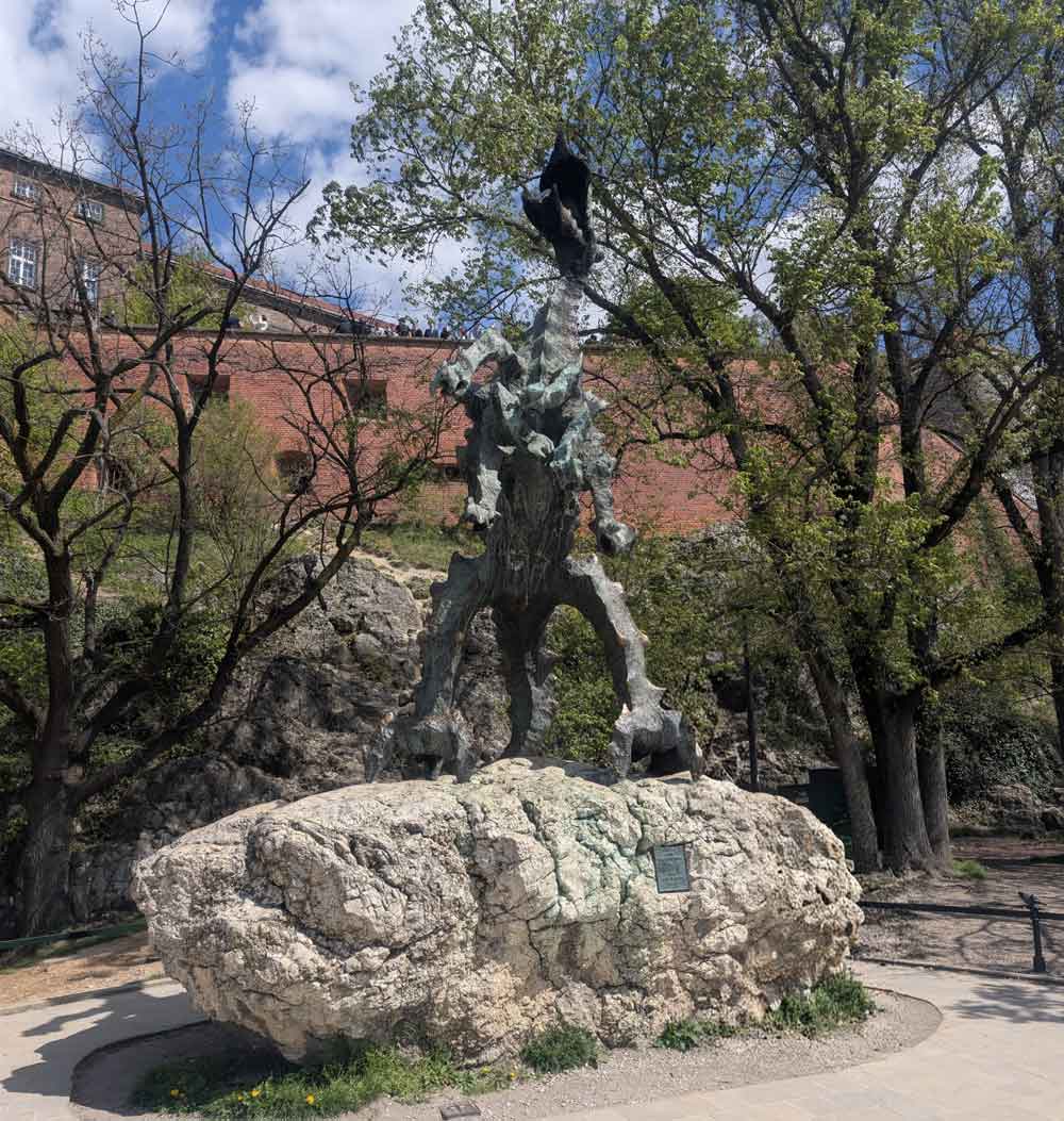 Sculpture of metal dragon on a rock in front of some trees with the castle in the background