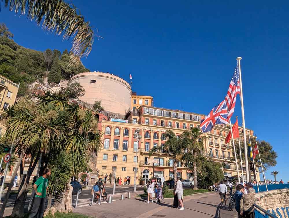 Hotel Suisse in background, with flags, people and palm trees in foreground