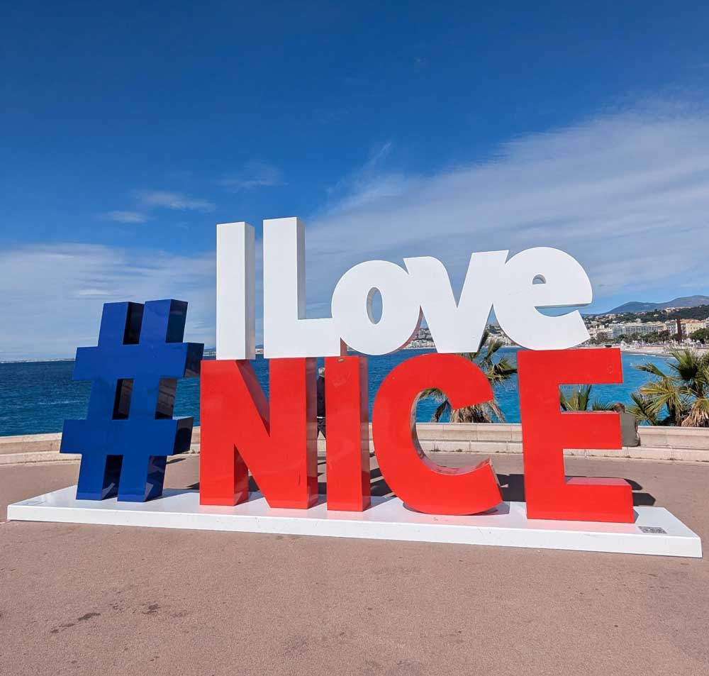 Large red, white and blue sign of #ILoveNice with sea in distant background