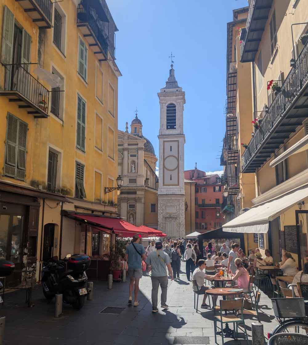 Old Town in Nice, with people sat outside cafes and cathedral tower in distance