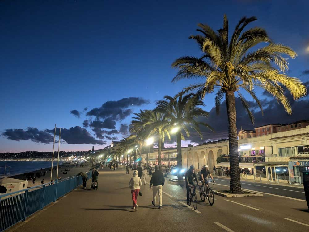 Promenade des Anglais in Nice at night. Palm-lined seafront promenade with walkers and cyclists