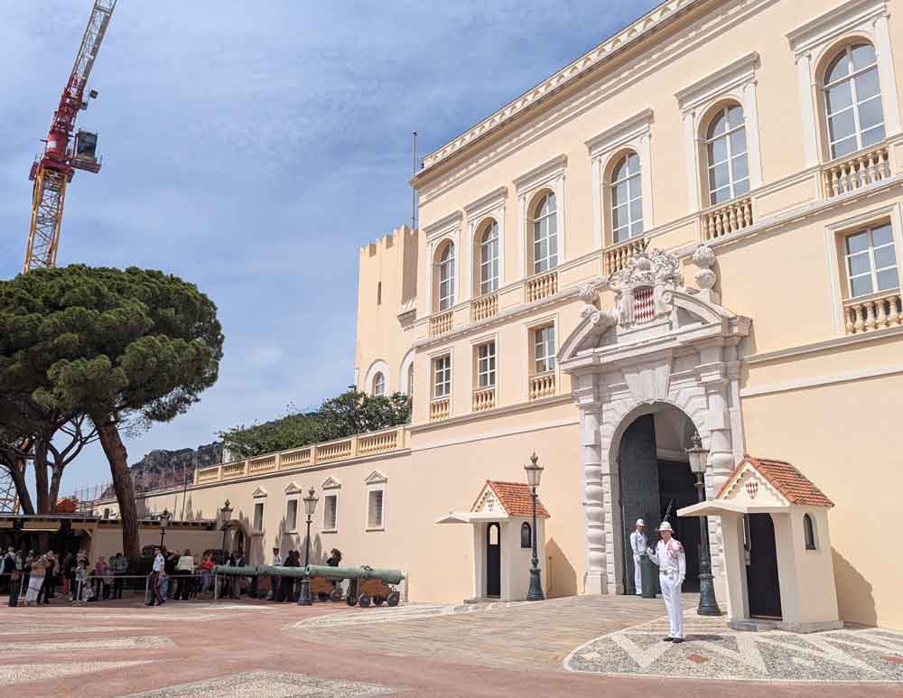 Guards in white uniform in front the Prince's Palace in Monaco. Single tree to the left with a crane behind.