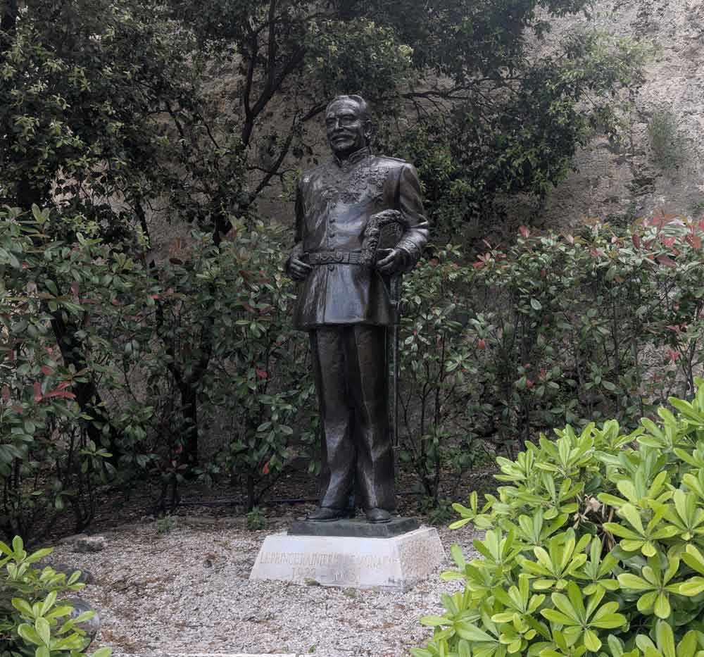 Bronze statue of Prince Rainer of Monaco in military uniform on plinth in front of bushes