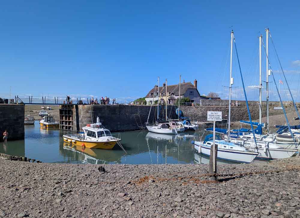 Historic harbour at Porlock Weir with boats bobbing in water and thatched cottages in background.