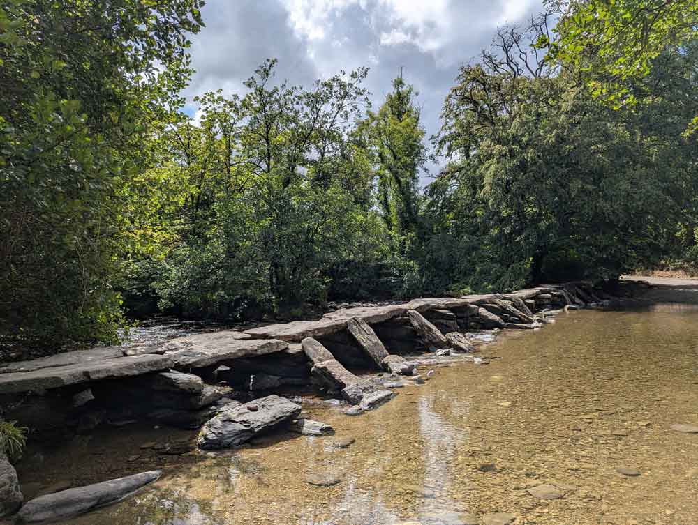 Ancient stone clapper bridge called Tarr Steps crossing river with trees in background