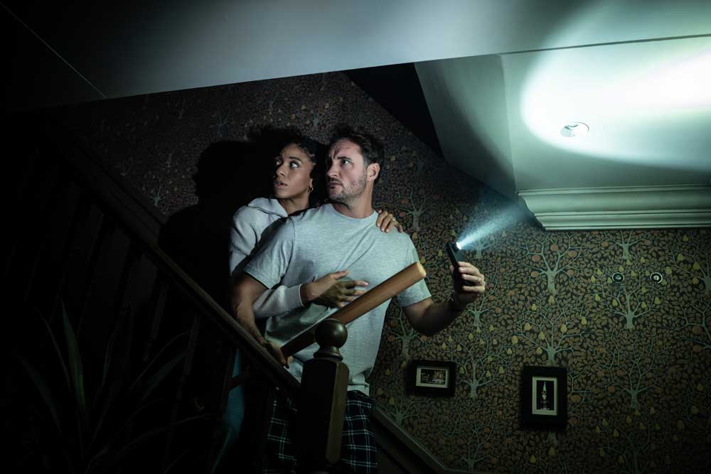 Couple creeping down stairs in the dark with a light and baseball bat