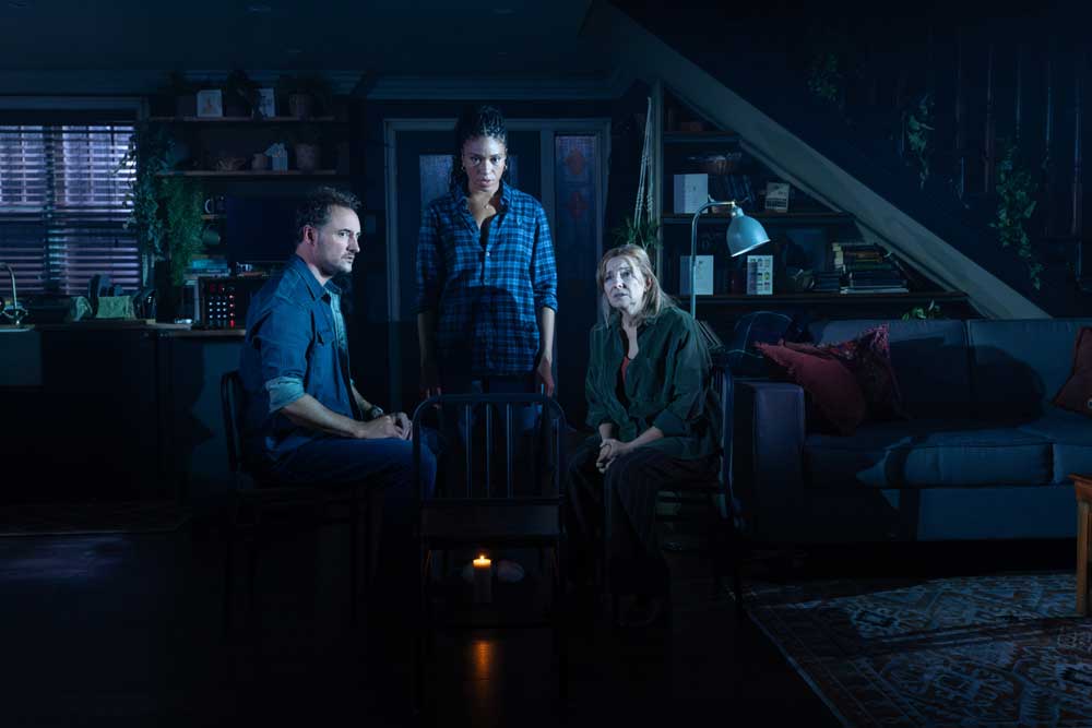 Three people in the house in dark, with 2 sitting and one standing