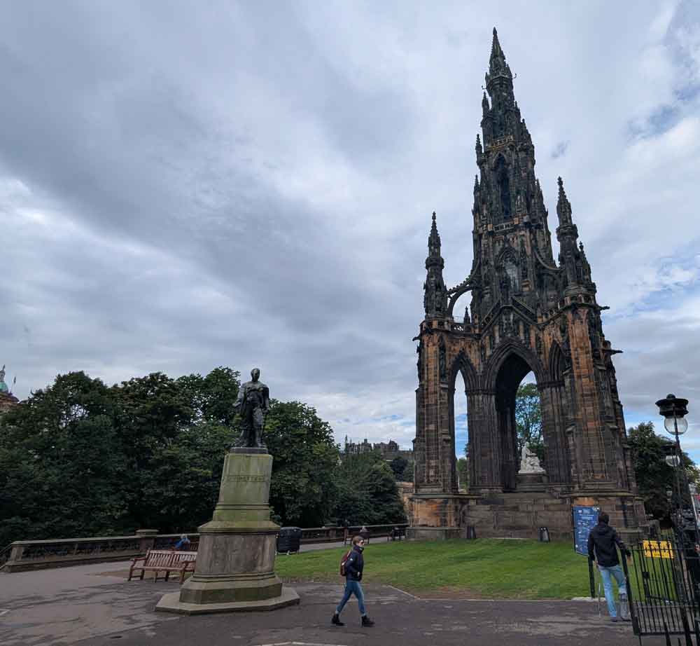 Gothic monument with small statue in front a couple of people walking about
