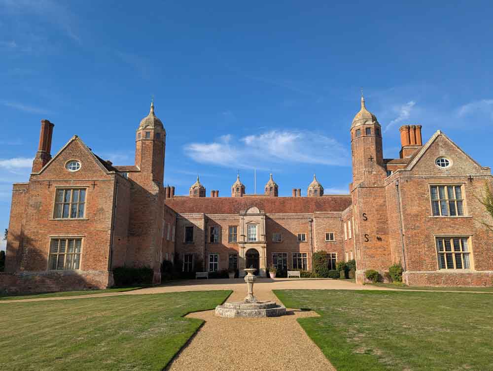 Red-bricked tudor mansion with lawn and sundial in front